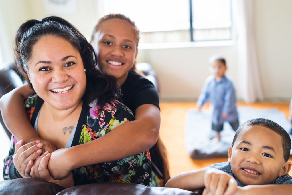 mother and her two children smiling at the camera, another child plays in the background