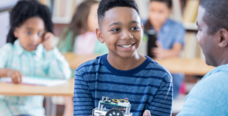young boy in classroom smiles at adult teacher