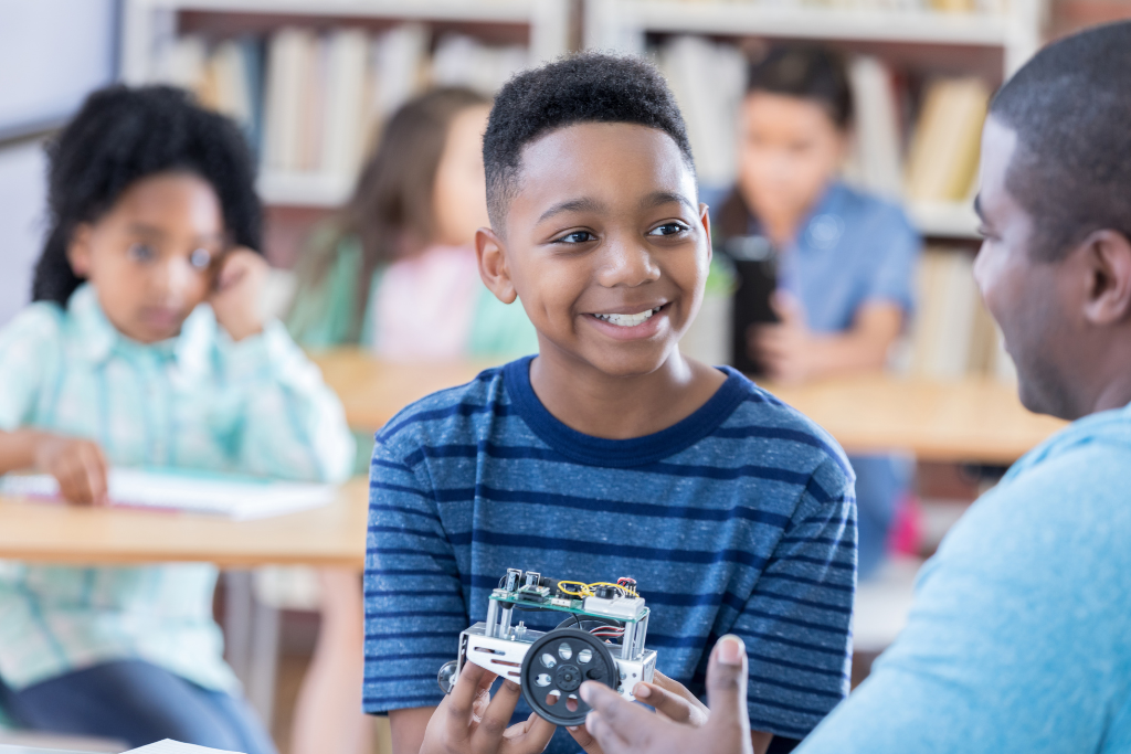 young boy in classroom smiles at adult teacher