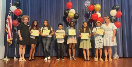 Students from Manatee Elementary and Daughtrey Elementary School on stage showing their scholarship certificates