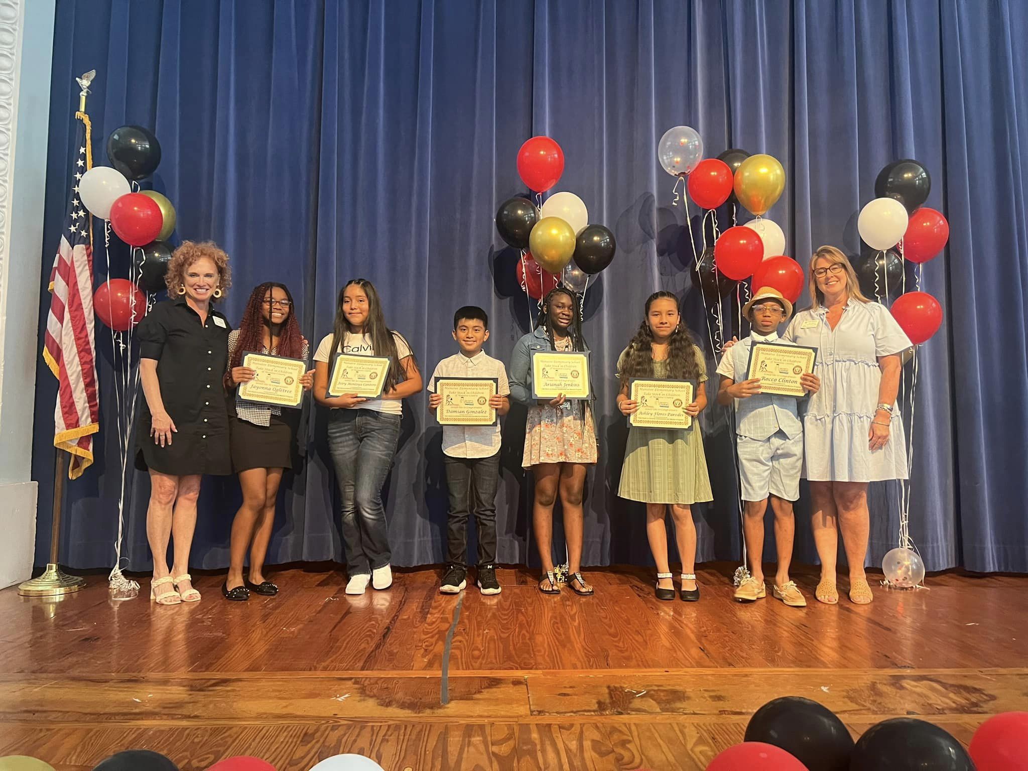 Students from Manatee Elementary and Daughtrey Elementary School on stage showing their scholarship certificates