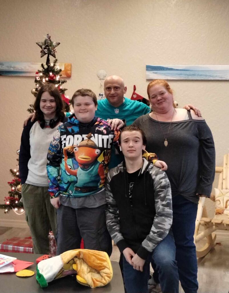 family of 5 smiling together in front of a Christmas tree